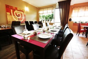 Restaurante com uma mesa comprida posta para refeições, cadeiras e uma grande pintura abstrata na parede.