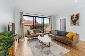 A modern living room with a sofa set, a coffee table, and a large window with a view of a brick building. - The Roundabout Rest - Heart of Wagga (Wagga Wagga)