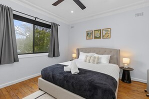 Une chambre à coucher avec un lit, deux lampes de chevet, une fenêtre avec des rideaux et trois tableaux encadrés accrochés au mur.