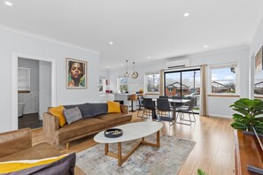 A modern living room with a sofa, coffee table, and dining area. - The Roundabout Rest - Heart of Wagga (Wagga Wagga)
