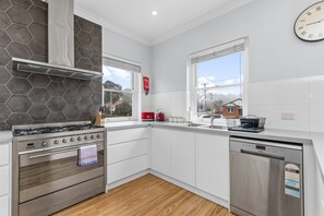 A modern kitchen with a gas stove, oven, dishwasher, and a window with a view of the outside. - The Roundabout Rest - Heart of Wagga (Wagga Wagga)