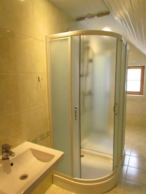 Un baño con ducha de vidrio, lavamanos y paredes con azulejos.