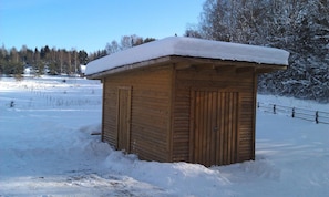 A wooden structure with a snow-covered roof, surrounded by a snowy landscape and trees.