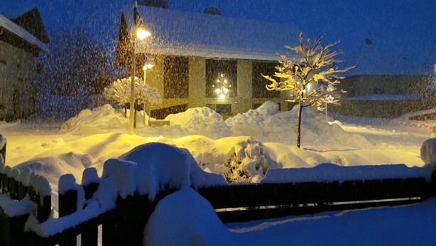 Paisaje nevado con un edificio, un árbol cubierto de nieve y una cerca.