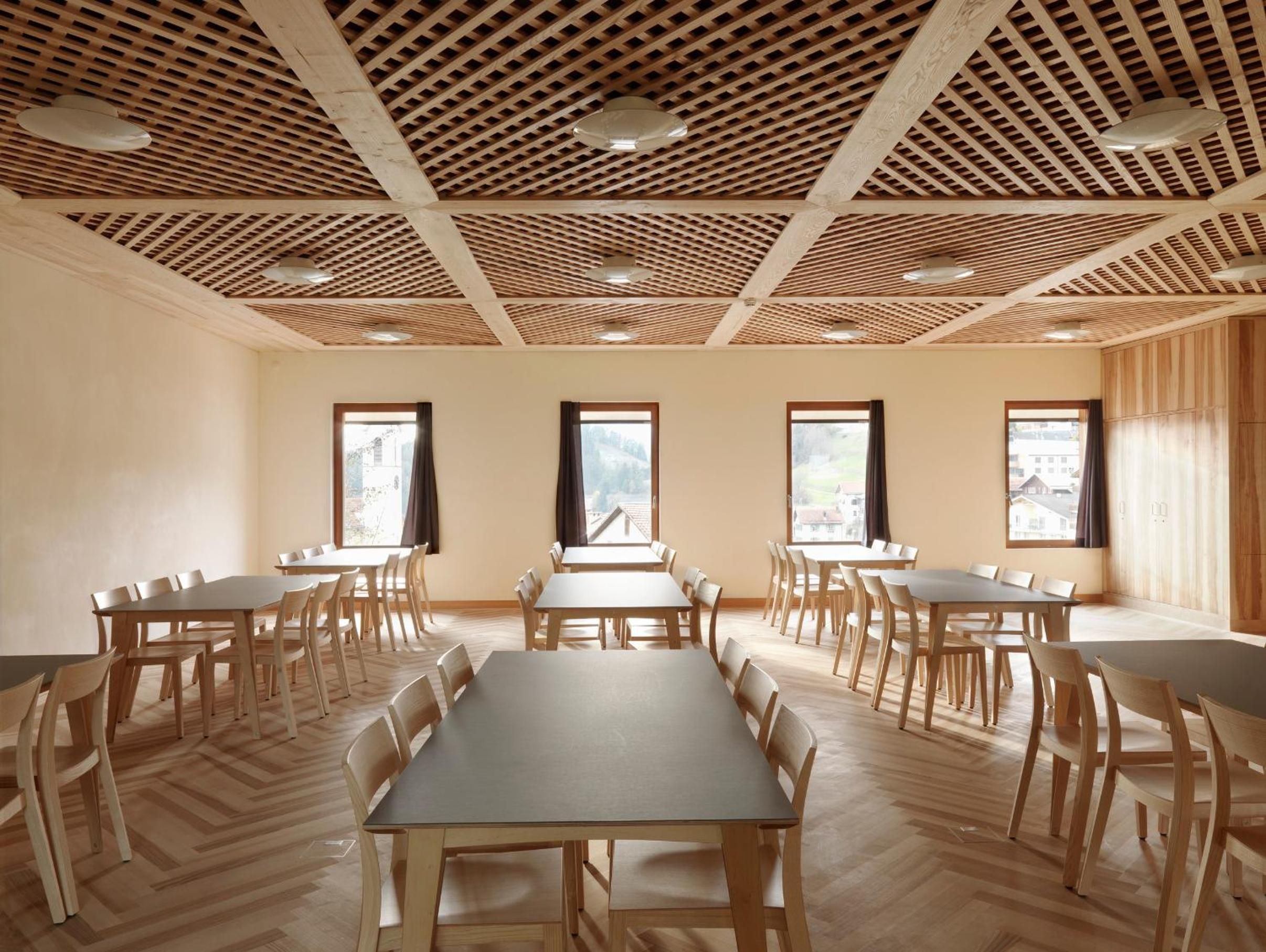 Une salle de conférence dotée de plusieurs tables et chaises, d’un plancher en bois et d’un plafond orné d’un motif en réseau.