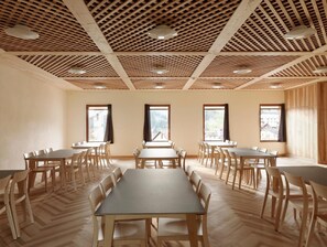 Un salón de conferencias con varias mesas y sillas, suelo de madera y techo con diseño de entramado.