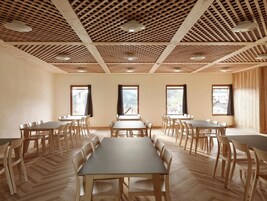 Un salón de conferencias con varias mesas y sillas, suelo de madera y techo con diseño de entramado.