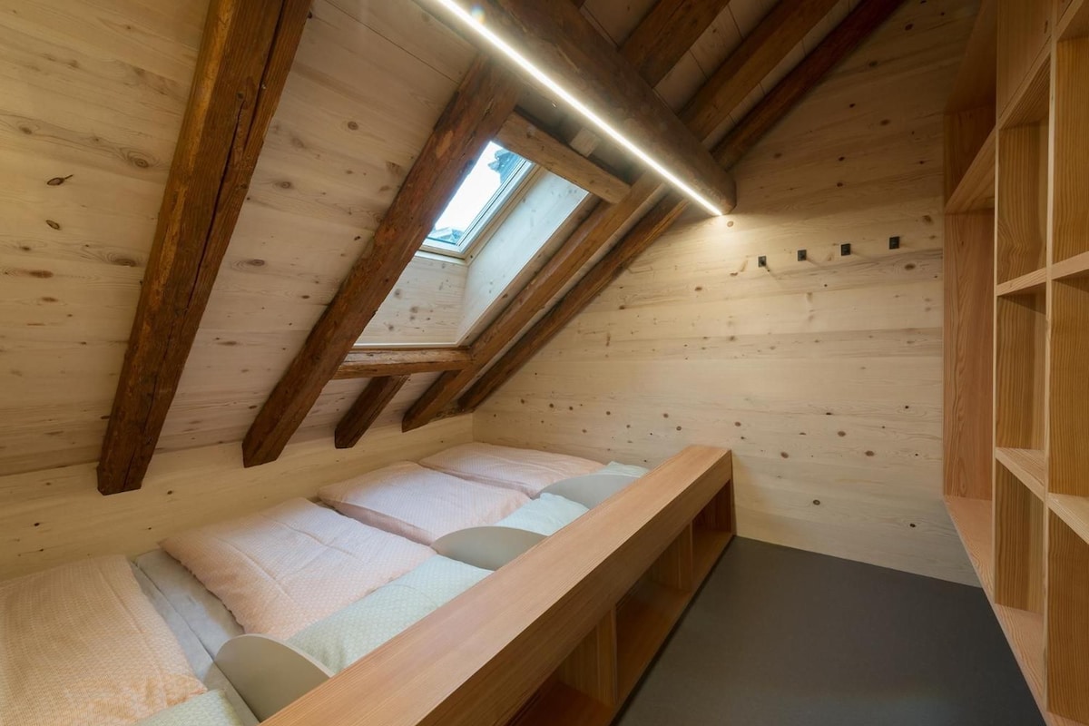 Ein Holzinnenraum mit schrägen Decken, einer Dachfensterkuppel und einer eingebauten Bank mit Kissen.