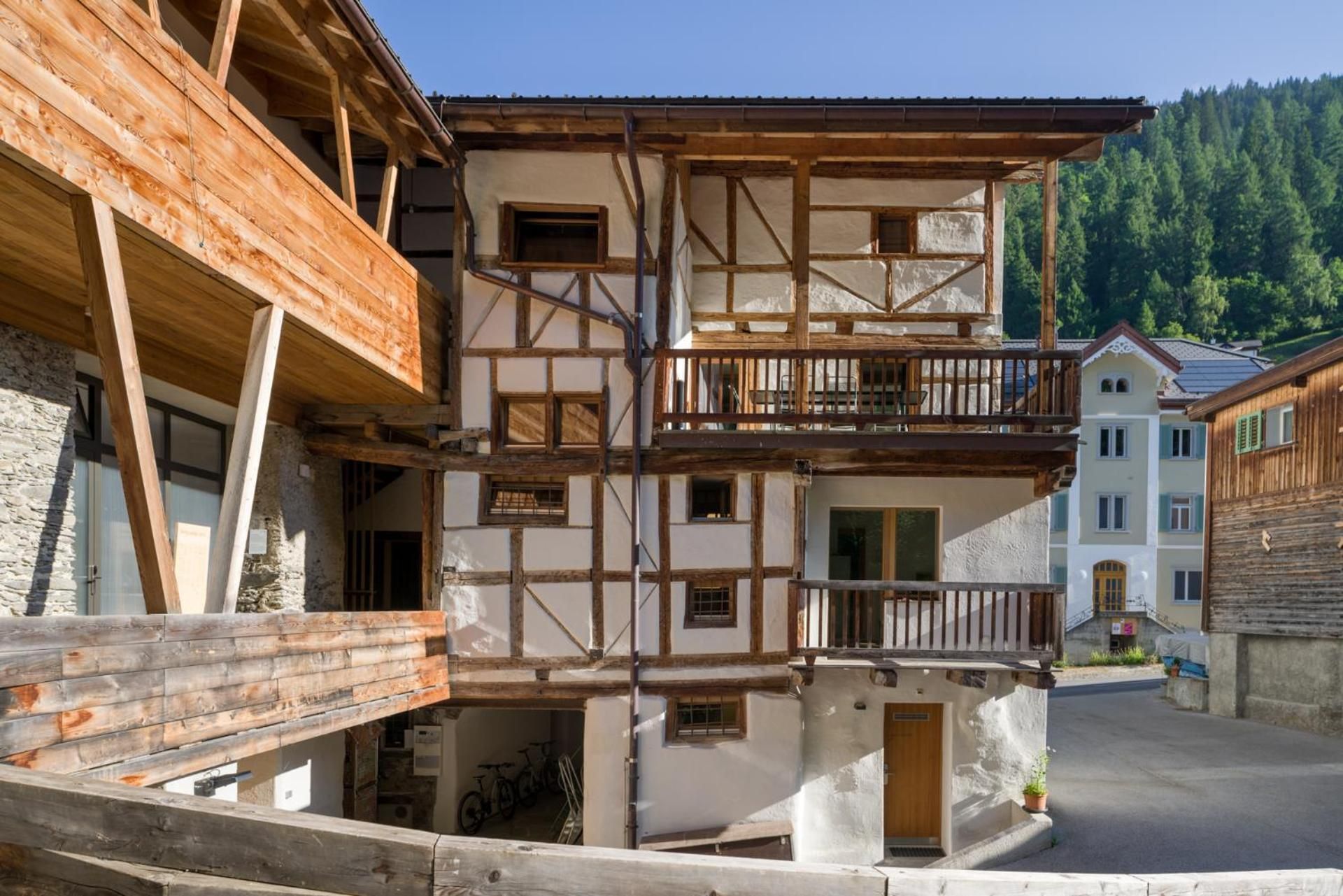 Un bâtiment traditionnel à colombages, doté d’un balcon, de murs en pierre et surplombant un paysage montagneux.
