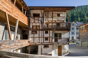 Un edificio tradicional con entramado de madera, balcón, paredes de piedra y montañas al fondo.