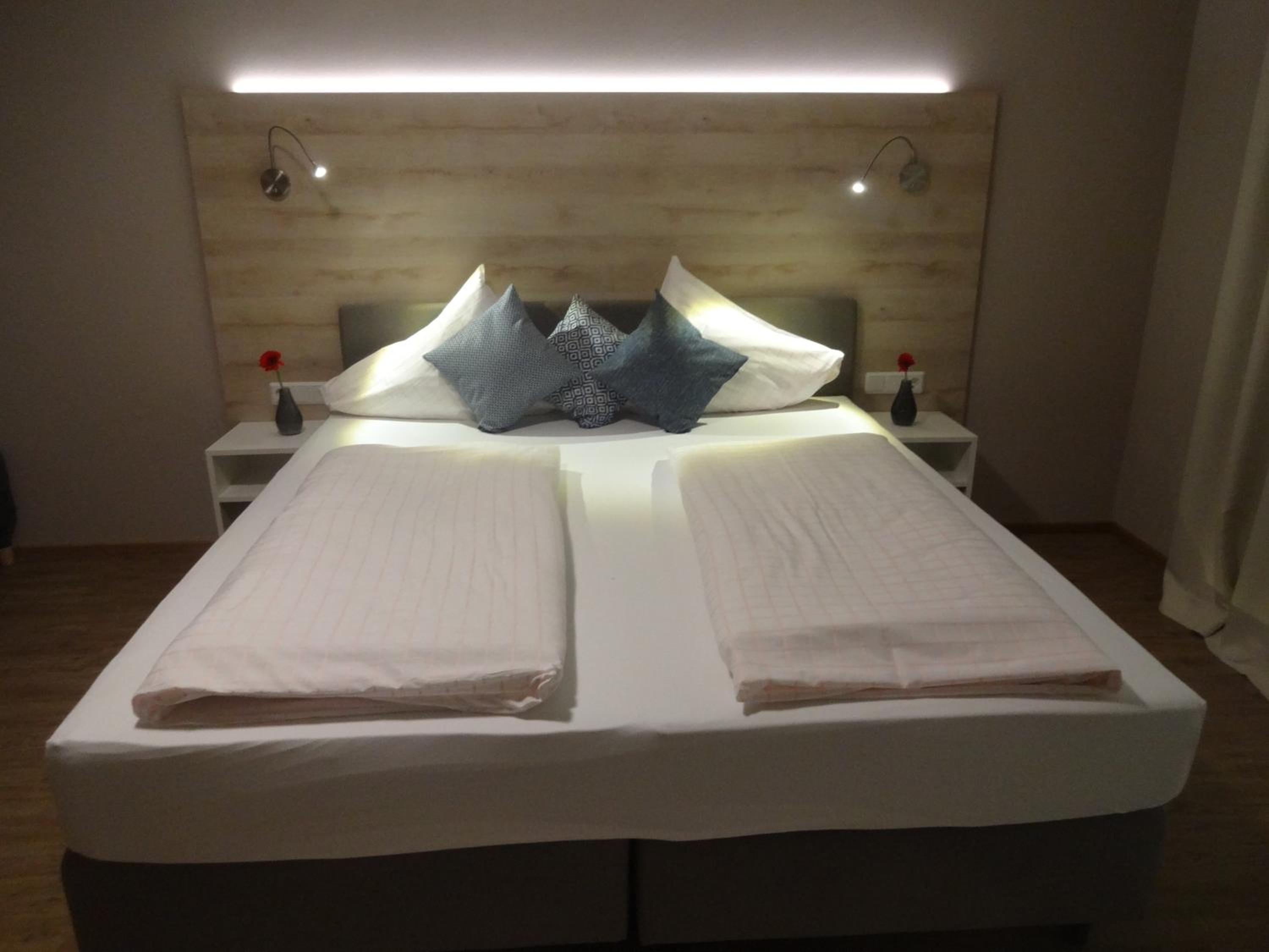Ein ordentlich bezogenes Bett mit einem Kopfteil, zwei Nachttischen und einer wandmontierten Leuchte.