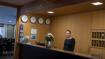 A reception desk with clocks indicating different time zones, a vase with flowers, and a sign above the desk reading 'RECEPTION'.