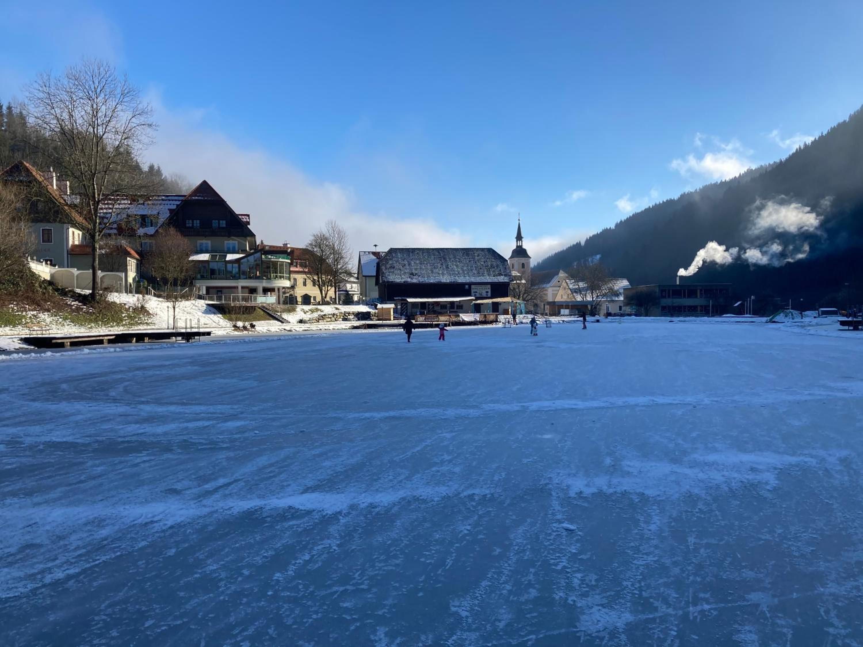 Ein zugefrorener See mit Gebäuden und einer Kirche im Hintergrund.