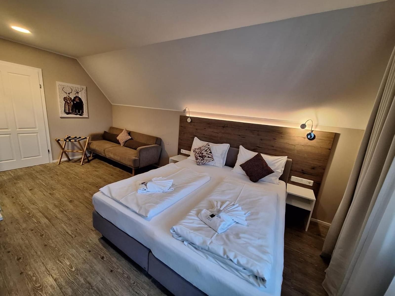 Un dormitorio con una cama grande, un sofá, cabecera de madera y una lámpara de pared.
