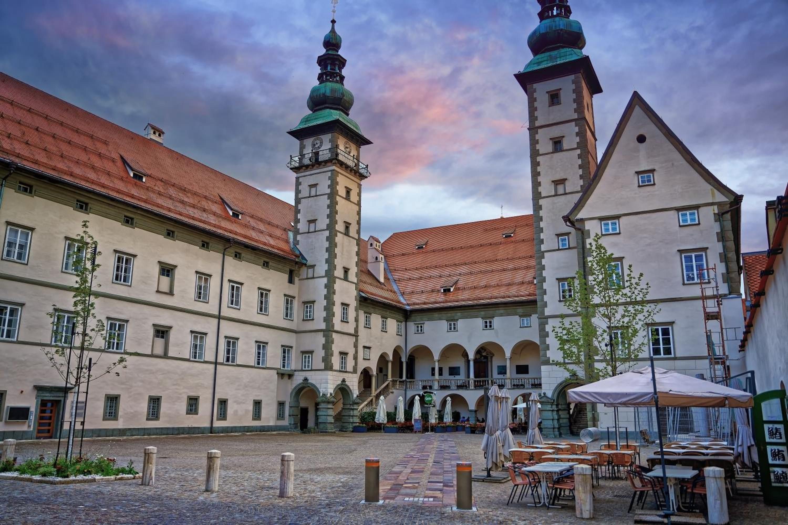 Ein Innenhof mit einem Gebäude, das einen Glockenturm und eine überdachte Sitzgelegenheit besitzt.