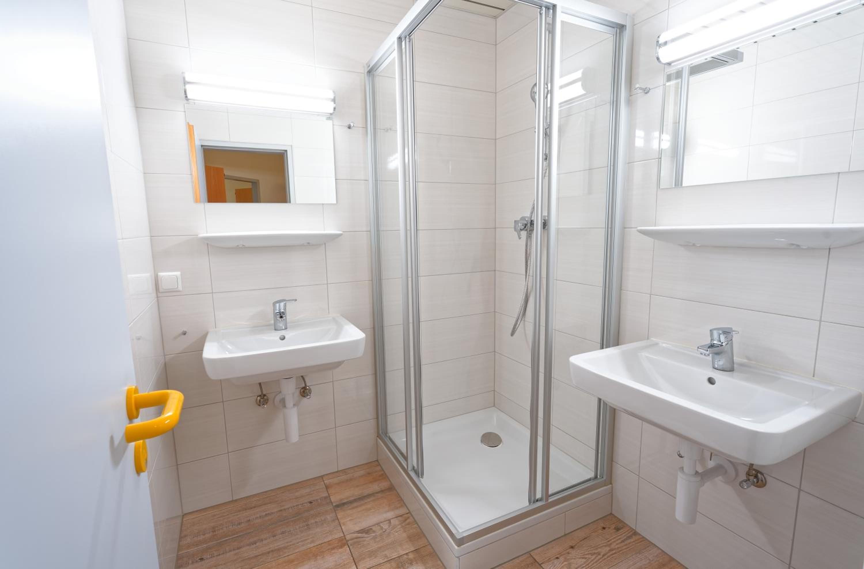 Ein modernes Badezimmer mit einer gläsernen Duschkabine, zwei Waschbecken und einem Spiegel über dem linken Waschbecken.