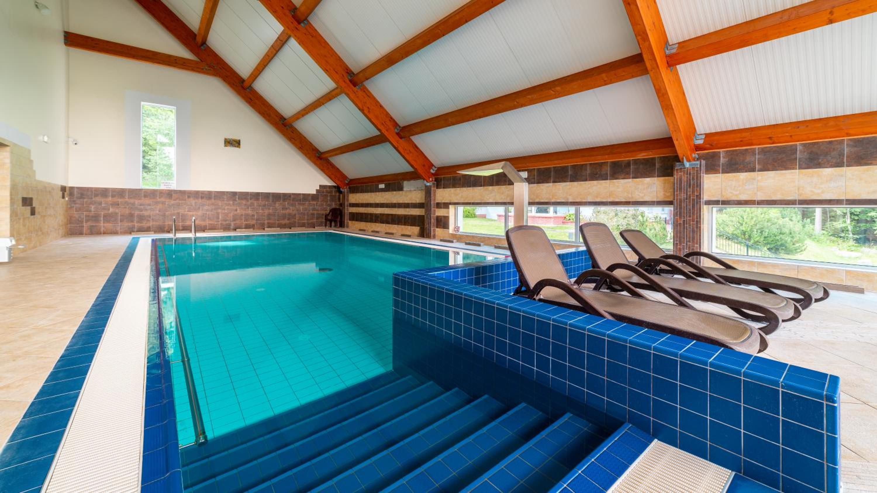 Una piscina interior con azulejos azules, vigas de madera y sillones de descanso.