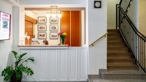 Un mostrador de recepción con fotografías enmarcadas, un reloj y una escalera con barandilla negra.