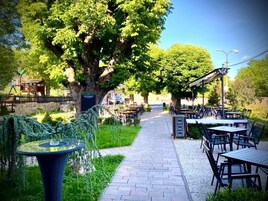 Un área de estar al aire libre con mesas y sillas, un sendero y un árbol grande.