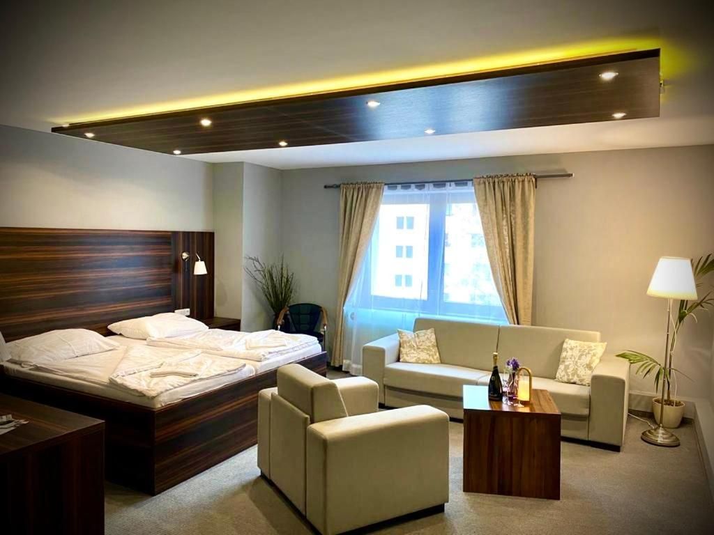 Una habitación de hotel con una cama, dos sofás, una mesita de centro y una ventana con cortinas.