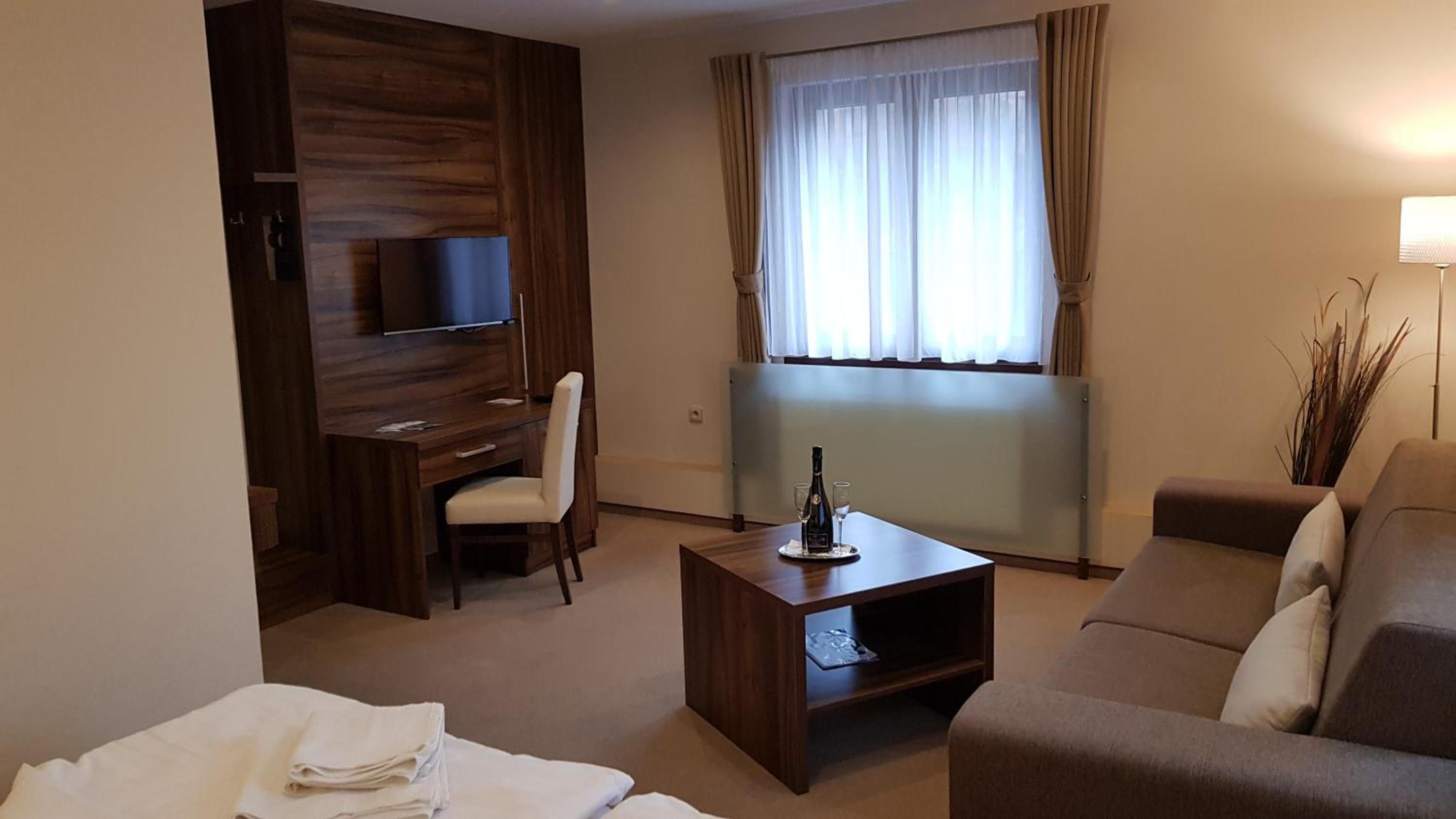Ein Hotelzimmer mit einem Holztisch, einem Fernseher, einer Couch und einem Fenster mit Vorhängen.