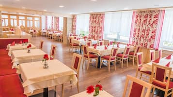 A restaurant with multiple tables and chairs, arranged in a spacious layout with large windows and curtains.