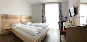 A hotel room with a double bed, a desk with a chair, a television, and a window with curtains. - Florianihof (Miesenbach bei Birkfeld)