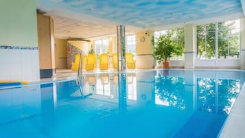 An indoor swimming pool with clear blue water, yellow chairs, and potted plants.