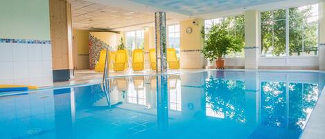 An indoor swimming pool with clear blue water, yellow chairs, and potted plants.