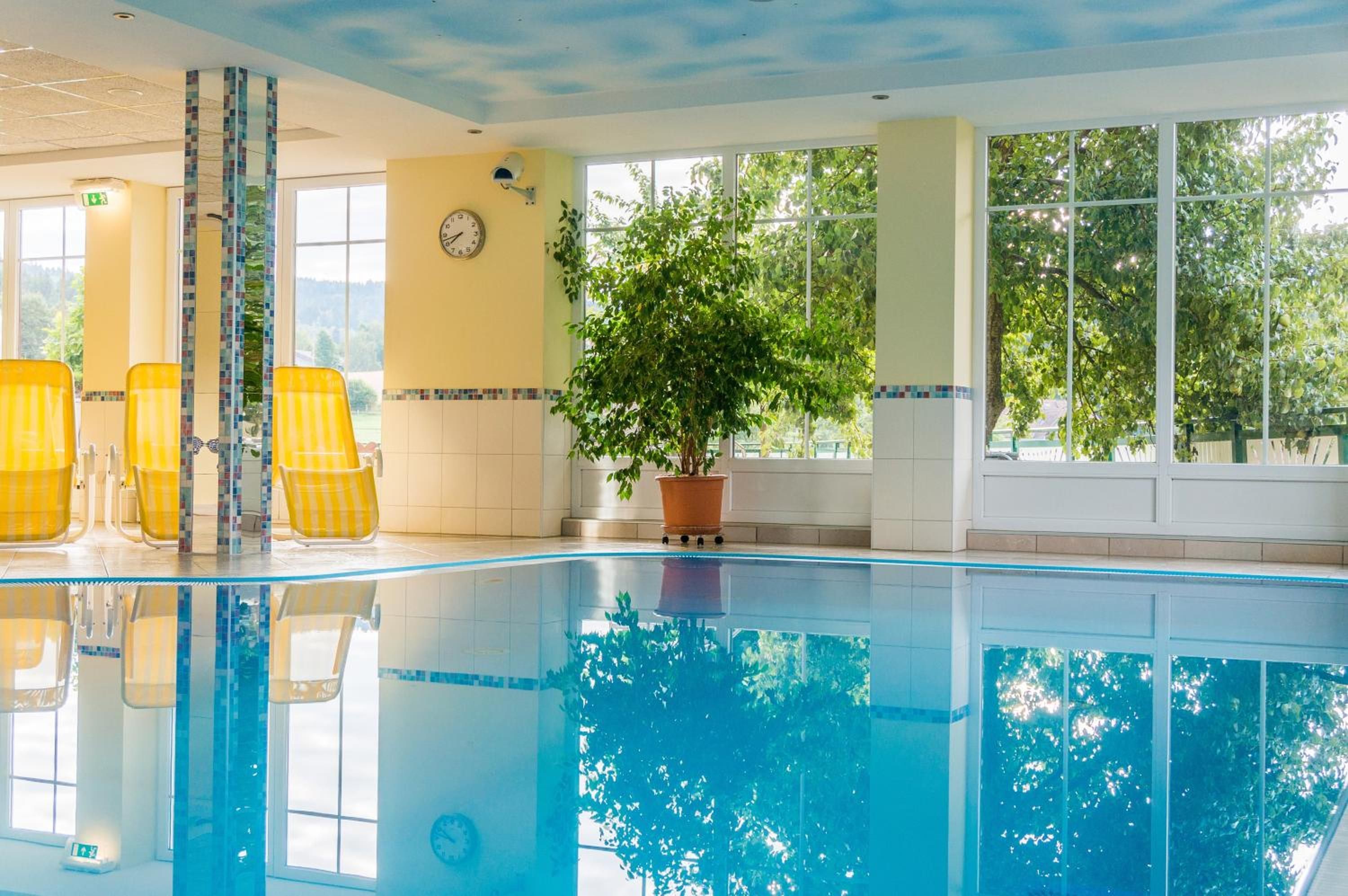 Una piscina con sillas amarillas, una planta en maceta y un reloj en la pared.