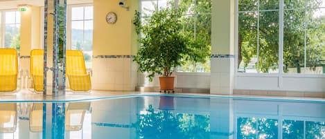 A swimming pool with yellow chairs, a potted plant, and a clock on the wall.