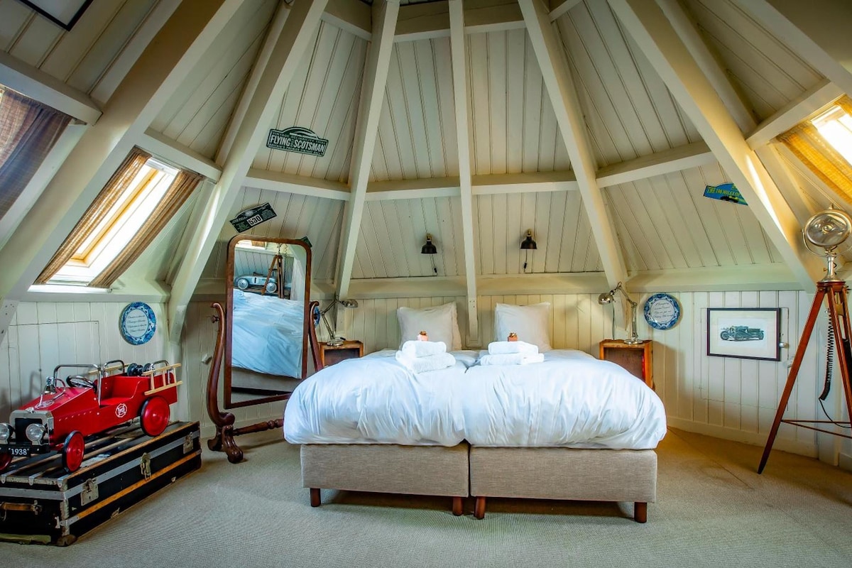 A bedroom with a large bed, a vintage car, and a telescope.