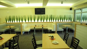 A restaurant with booths and tables, a flat-screen TV mounted on the wall, and a row of green plants along the back wall. - Hotel Kaskada (Ledeč nad Sázavou)