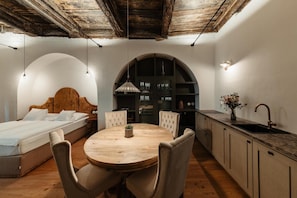 Un dormitorio compacto con cama, una mesa redonda con sillas, una cocina con pileta y placares, y un jarrón decorativo.