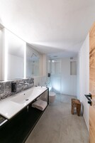 Un baño moderno con un espejo grande, dos lavamanos, una ducha y un taburete de madera.