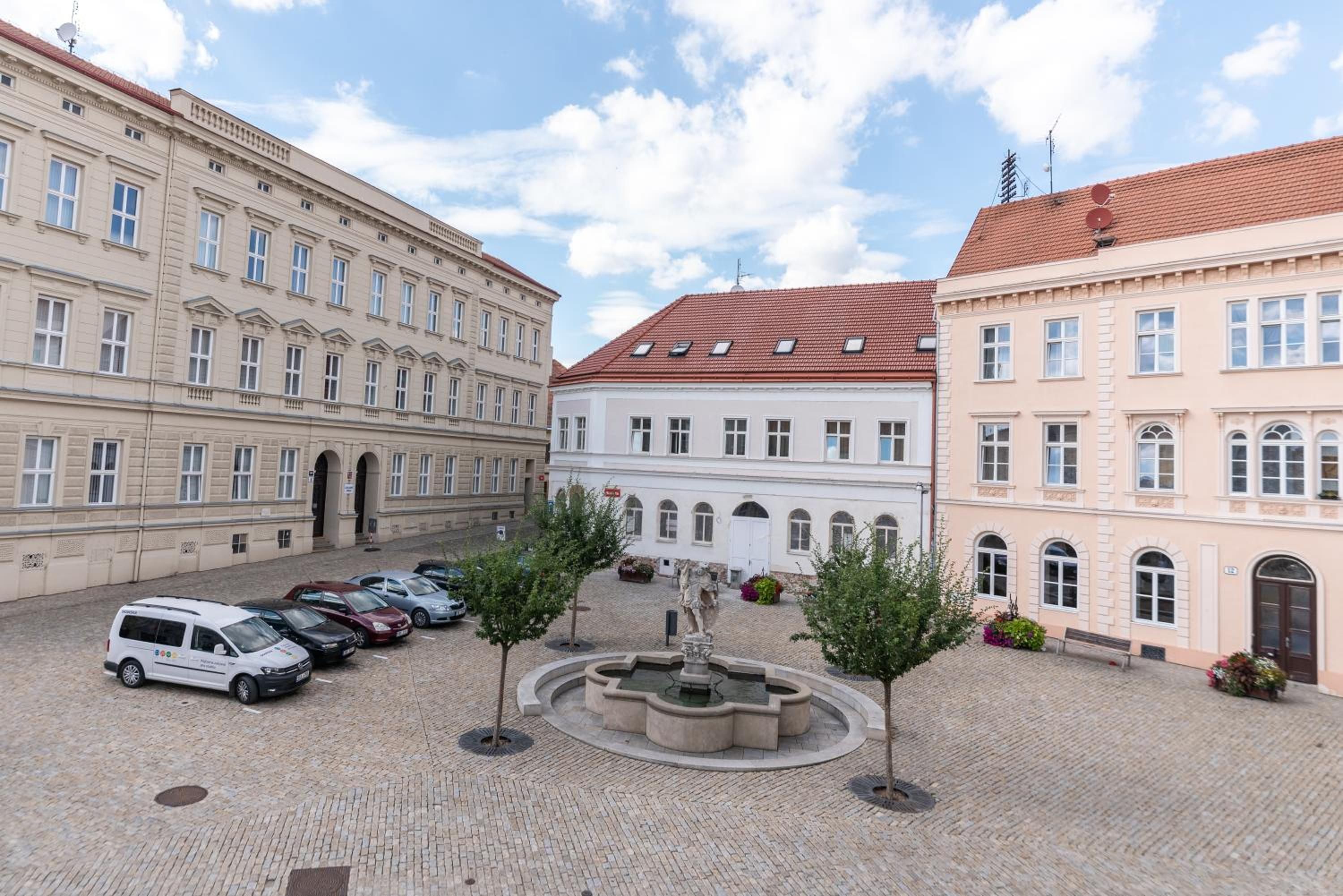 A courtyard with a fountain, surrounded by historic buildings with multiple windows and a red-tiled roof.