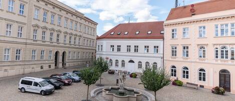 A courtyard with a fountain, surrounded by historic buildings with multiple windows and a red-tiled roof.