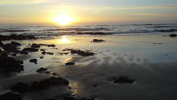 A beach with rocks and sand, and the sun is setting in the background.