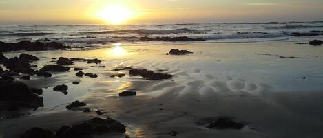 A beach with rocks and sand, and the sun is setting in the background.