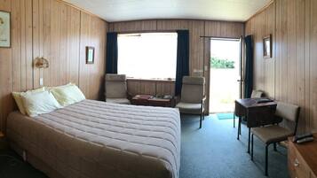 A room with a bed, two chairs, a desk, and a window.