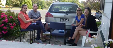 A group of people seated outside a building with a parked car in the background.
