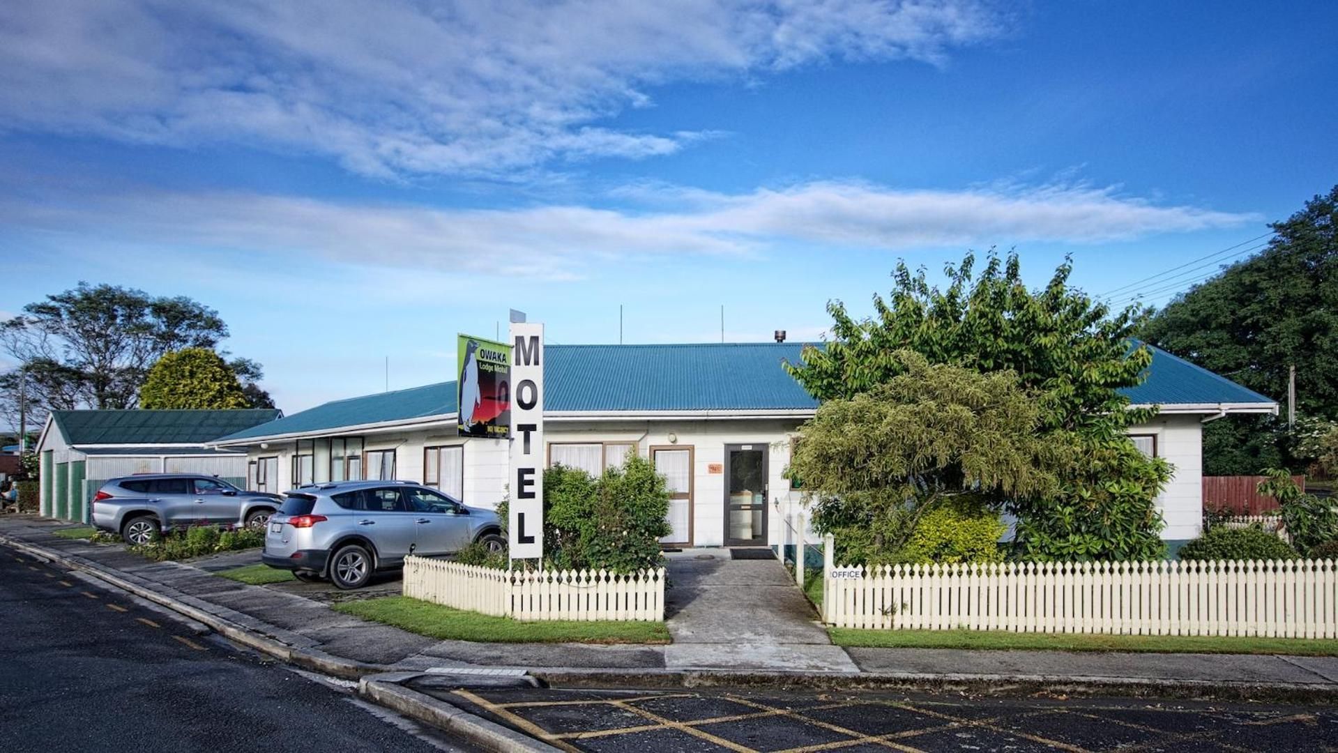 A motel with a green roof, a white picket fence, and a signboard.