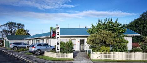 A motel with a green roof, a white picket fence, and a signboard.