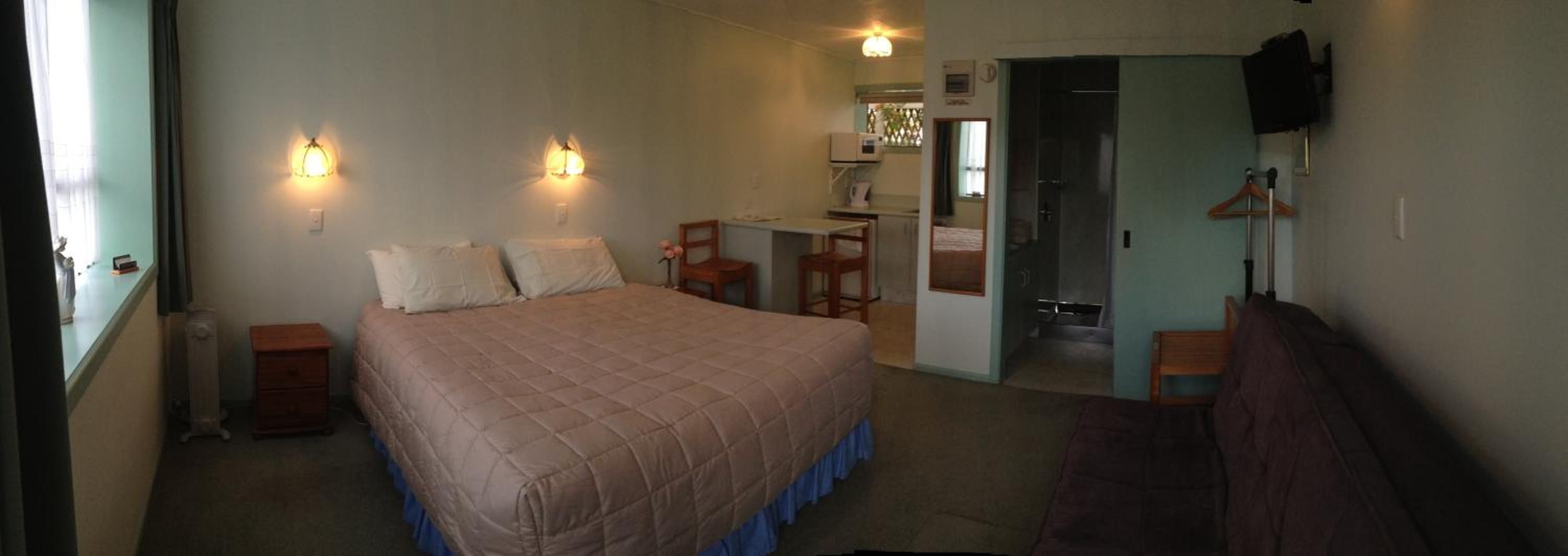 A bedroom with a bed, bedside tables, a desk, and a chair. There is a television mounted on the wall.