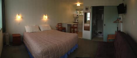 A bedroom with a bed, bedside tables, a desk, and a chair. There is a television mounted on the wall.