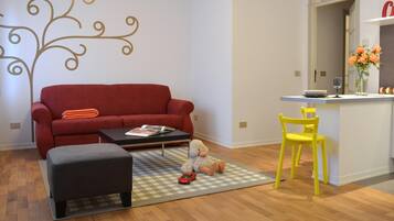 Ein Wohnzimmer mit einem roten Sofa, einem schwarzen Hocker, einem karierten Teppich, einem gelben Sessel und einem Kuscheltier auf dem Teppich.