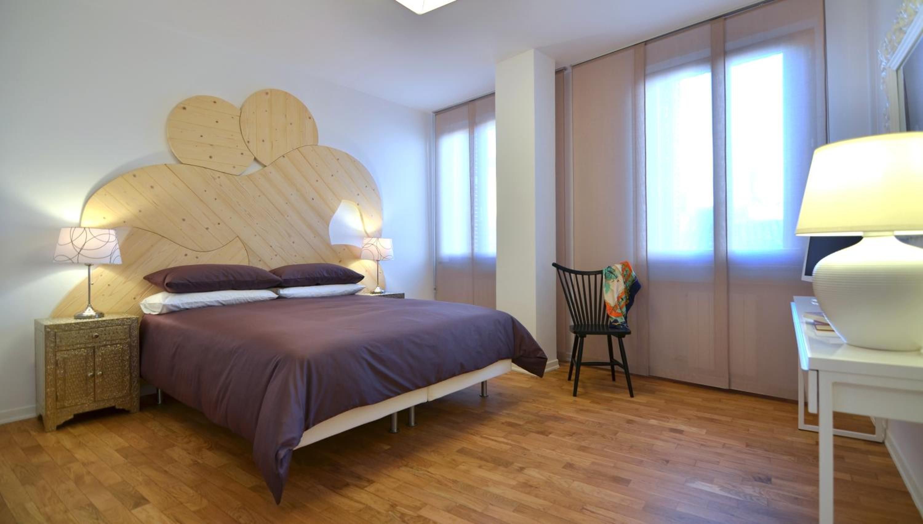 A bedroom with a bed, two bedside tables, a chair, and a desk with a lamp.
