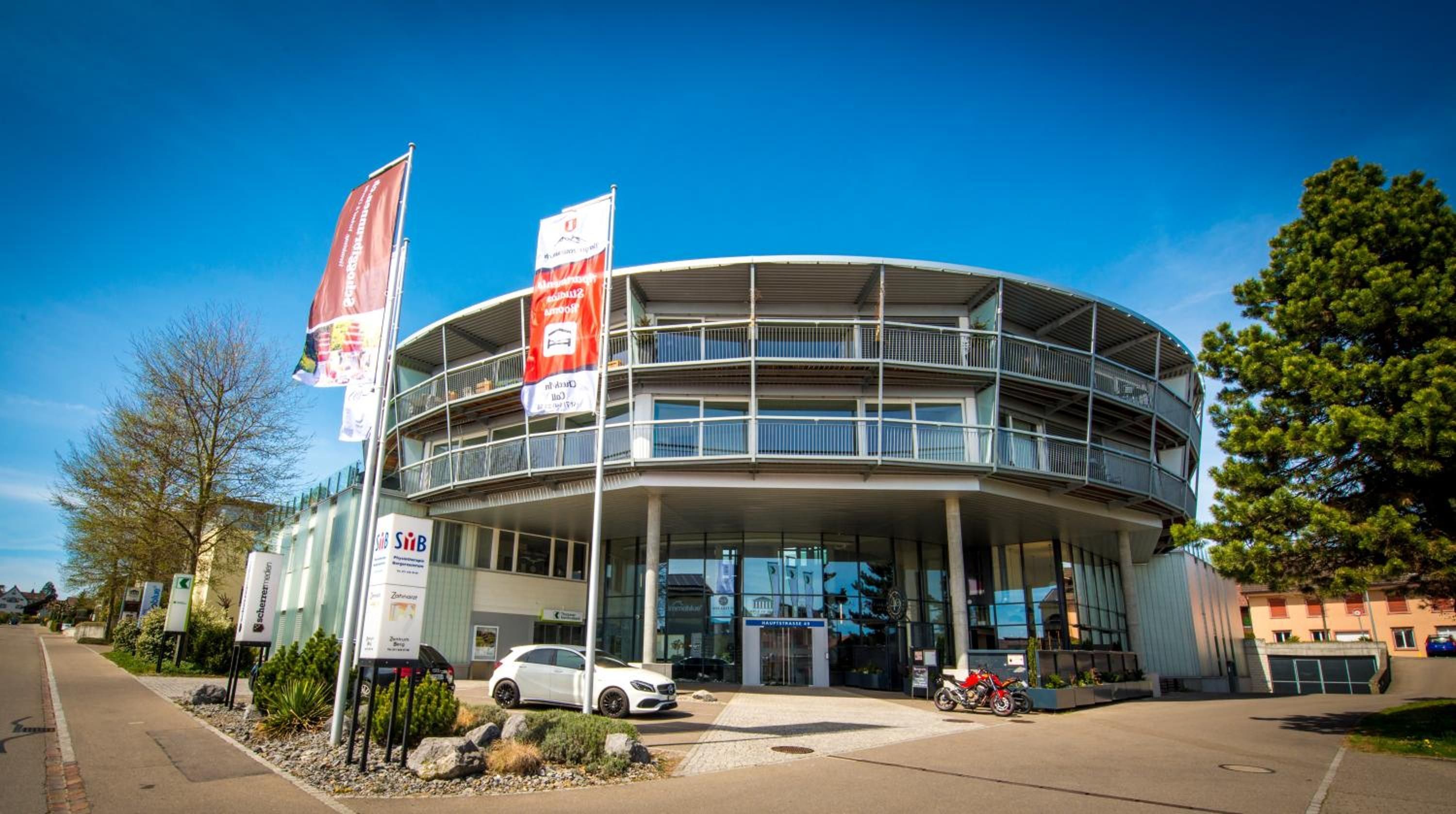 Ein modernes Gebäude mit einer geschwungenen Fassade und mehreren Balkonen, vor der ein Auto geparkt ist.