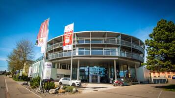 Ein modernes Gebäude mit einer geschwungenen Fassade und mehreren Balkonen, vor der ein Auto geparkt ist.