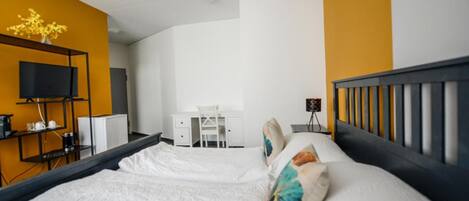 A hotel room with a bed, a desk, a chair, a TV, and a small table with a lamp.